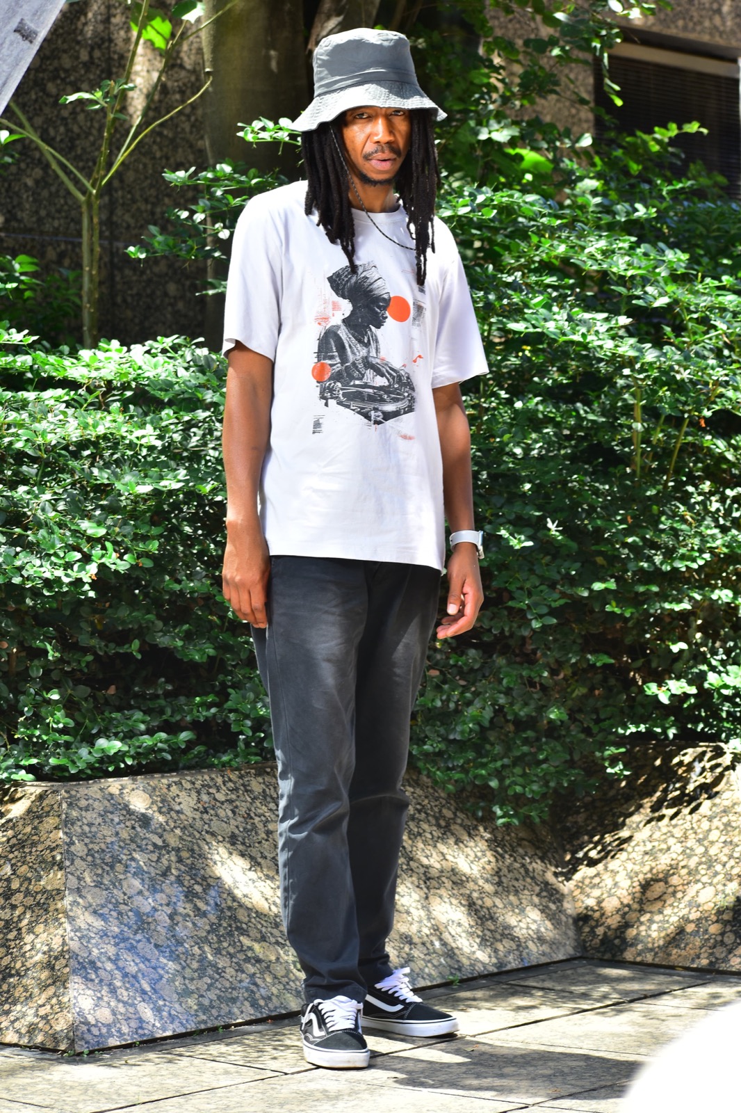 Darkie in a bucket hat and graphic tee among green foliage