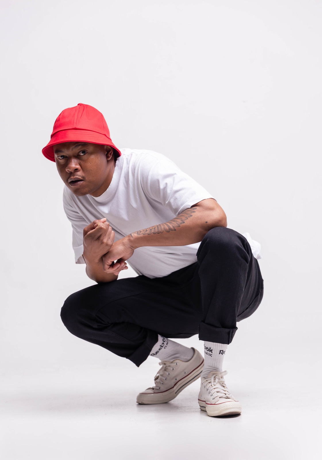 Mthizo crouching in a red hat and white tee